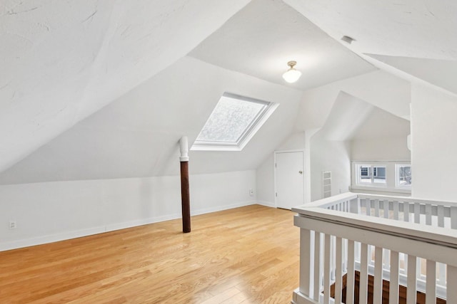 bonus room with wood-type flooring, lofted ceiling with skylight, and a healthy amount of sunlight