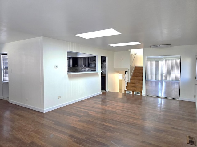 unfurnished living room featuring a skylight and dark hardwood / wood-style flooring