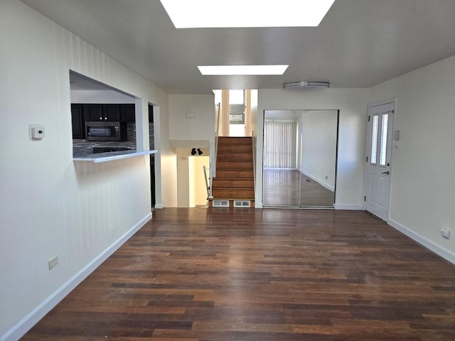 unfurnished living room featuring dark hardwood / wood-style flooring and a skylight