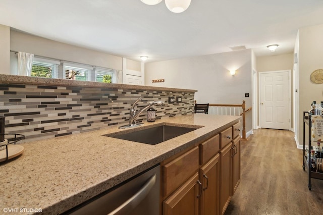 kitchen with backsplash, light stone counters, sink, hardwood / wood-style flooring, and dishwasher