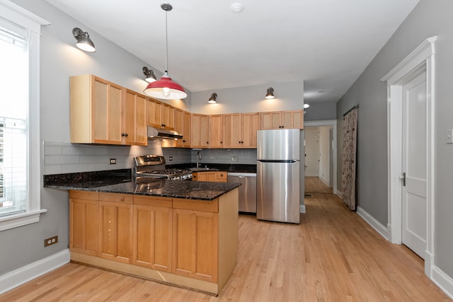 kitchen featuring stainless steel appliances, kitchen peninsula, backsplash, and light wood-type flooring