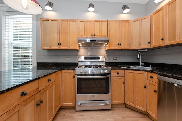 kitchen with sink, backsplash, stainless steel appliances, dark stone counters, and light hardwood / wood-style floors