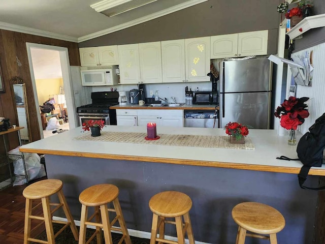 kitchen with crown molding, stainless steel appliances, white cabinetry, lofted ceiling, and a kitchen breakfast bar