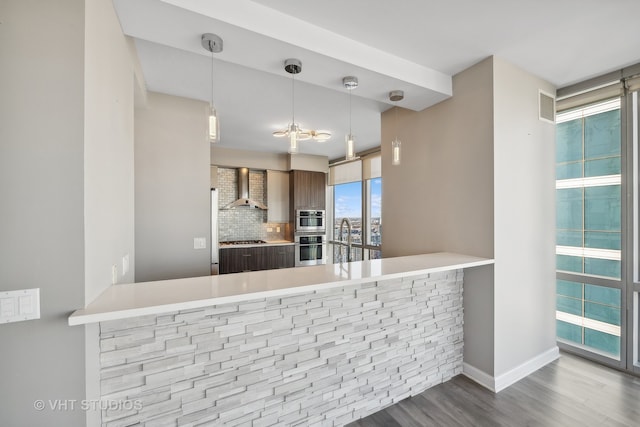 kitchen featuring wall chimney exhaust hood, kitchen peninsula, hardwood / wood-style flooring, and backsplash