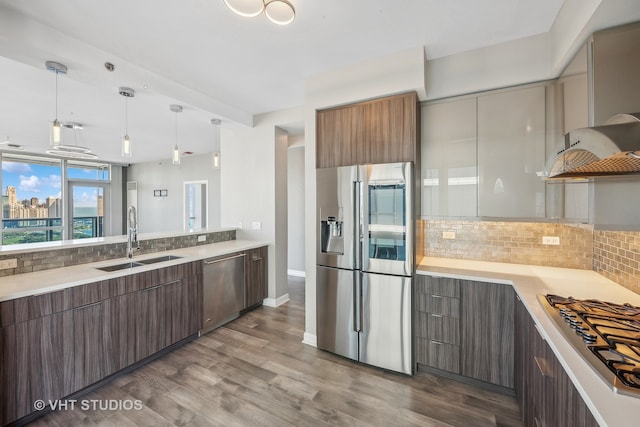 kitchen with tasteful backsplash, appliances with stainless steel finishes, sink, hanging light fixtures, and hardwood / wood-style floors