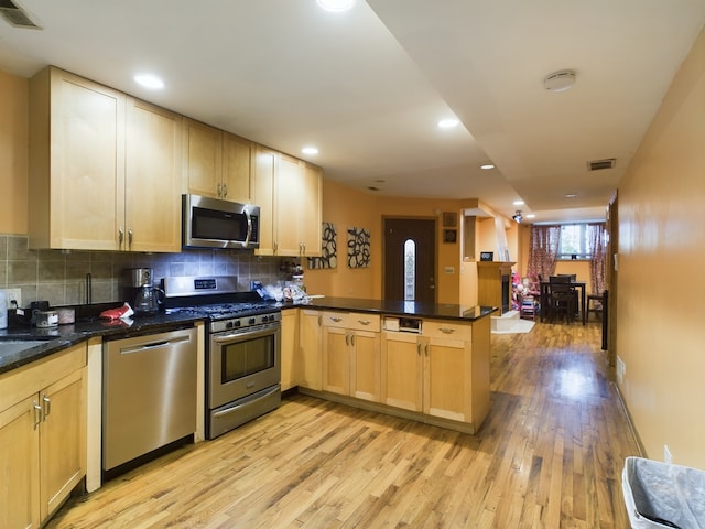 kitchen with dark stone countertops, light wood-type flooring, stainless steel appliances, light brown cabinets, and kitchen peninsula