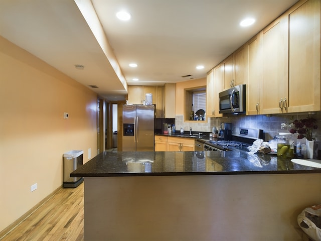 kitchen with stainless steel appliances, dark stone countertops, light wood-type flooring, and kitchen peninsula