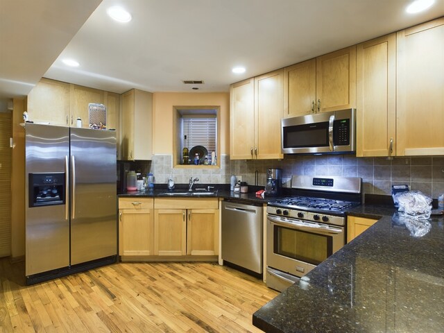 kitchen featuring light hardwood / wood-style flooring, backsplash, appliances with stainless steel finishes, sink, and dark stone counters