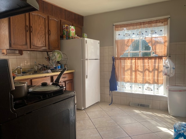 kitchen with white refrigerator, black range oven, light tile patterned floors, and range hood