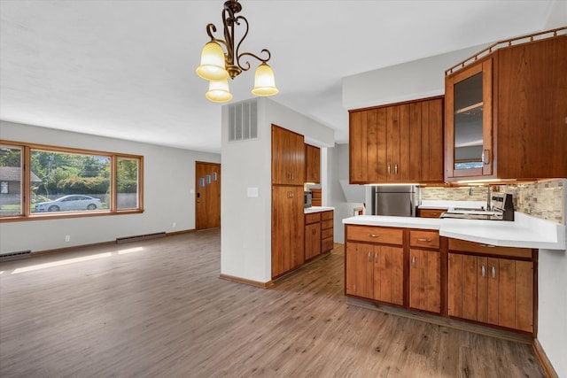 kitchen with hanging light fixtures, tasteful backsplash, stainless steel refrigerator, light hardwood / wood-style flooring, and a chandelier