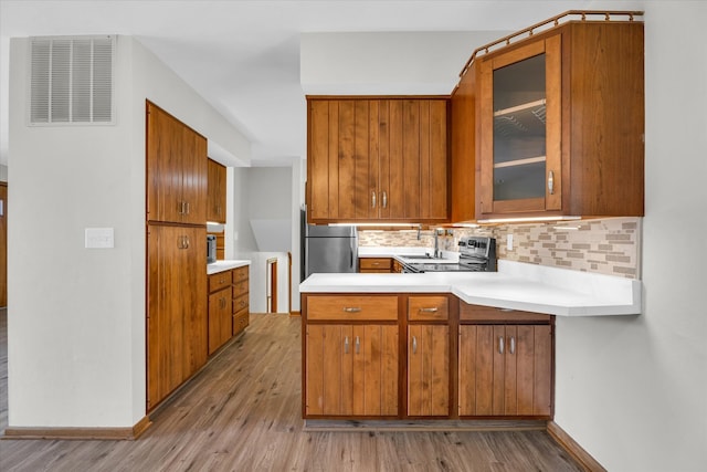 kitchen with stainless steel appliances, light hardwood / wood-style floors, kitchen peninsula, and tasteful backsplash