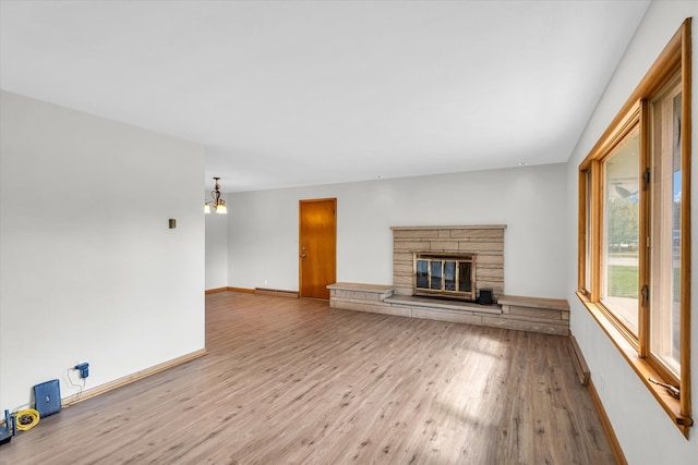 unfurnished living room featuring a stone fireplace, hardwood / wood-style flooring, and a chandelier