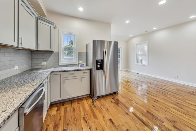 kitchen with stainless steel appliances, light stone countertops, decorative backsplash, gray cabinetry, and light hardwood / wood-style floors