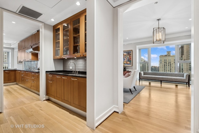 interior space featuring backsplash, an inviting chandelier, light hardwood / wood-style flooring, decorative light fixtures, and sink