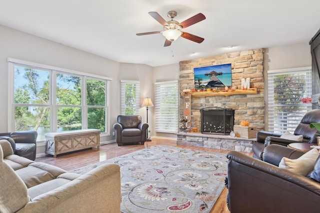 living room with a stone fireplace, wood-type flooring, and ceiling fan