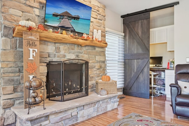 living room featuring a barn door, wood-type flooring, and a stone fireplace