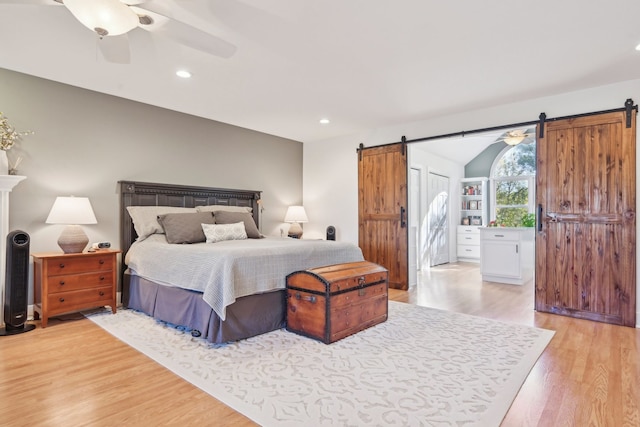 bedroom with a barn door, light hardwood / wood-style floors, and ceiling fan