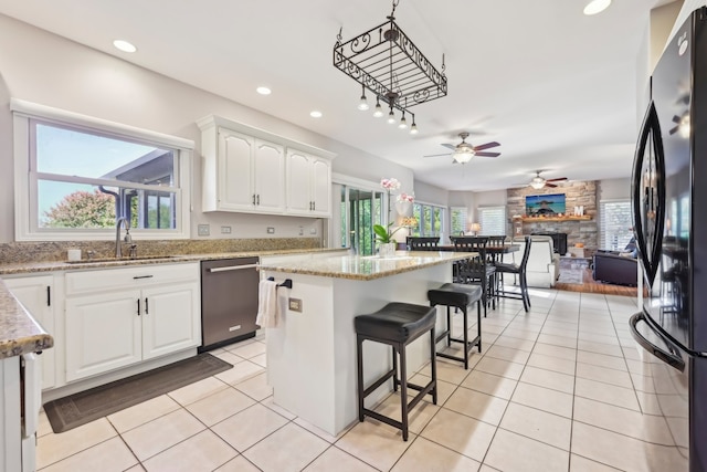 kitchen featuring white cabinets, black refrigerator, a stone fireplace, and dishwasher