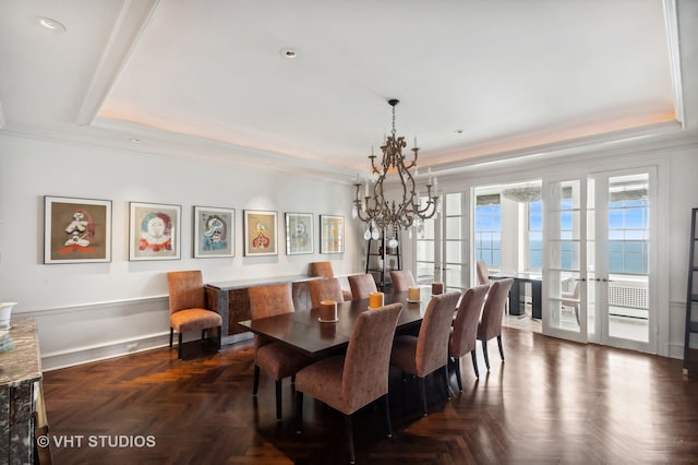 dining area featuring a raised ceiling, dark parquet floors, french doors, an inviting chandelier, and a water view