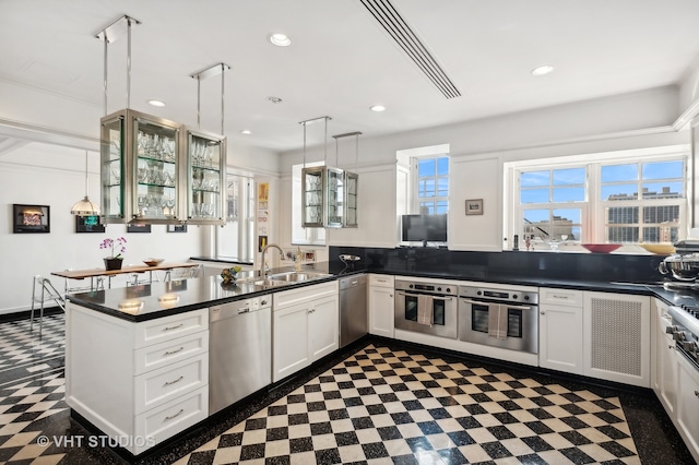 kitchen with a healthy amount of sunlight, hanging light fixtures, stainless steel appliances, and white cabinets