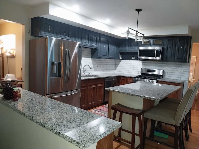 kitchen with backsplash, hardwood / wood-style flooring, appliances with stainless steel finishes, light stone countertops, and sink