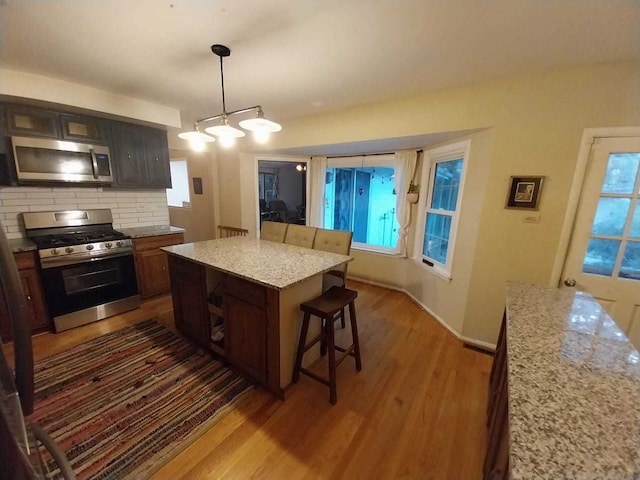 kitchen featuring a kitchen island, dark hardwood / wood-style floors, light stone countertops, a kitchen breakfast bar, and appliances with stainless steel finishes