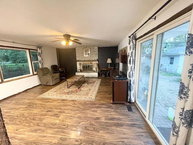 living room featuring a wall mounted AC, a brick fireplace, wood-type flooring, and ceiling fan