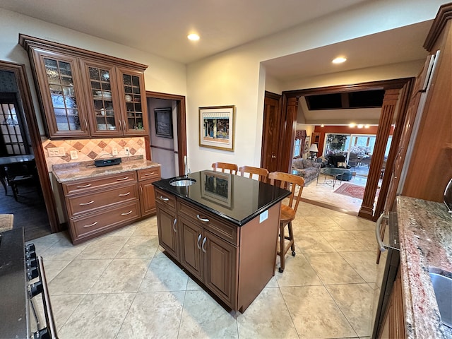 kitchen featuring a breakfast bar area, tasteful backsplash, a center island, stove, and dark stone countertops