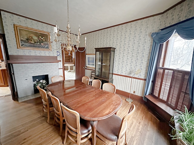 dining room with a chandelier, ornamental molding, light hardwood / wood-style floors, and a brick fireplace