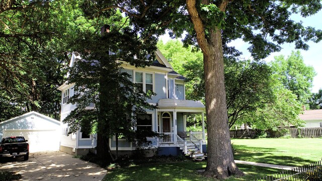 victorian house with a garage, covered porch, a front lawn, and an outbuilding