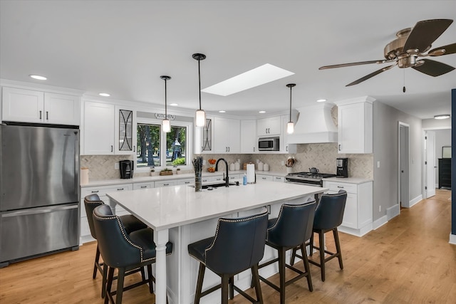 kitchen with premium range hood, a skylight, stainless steel appliances, and white cabinets