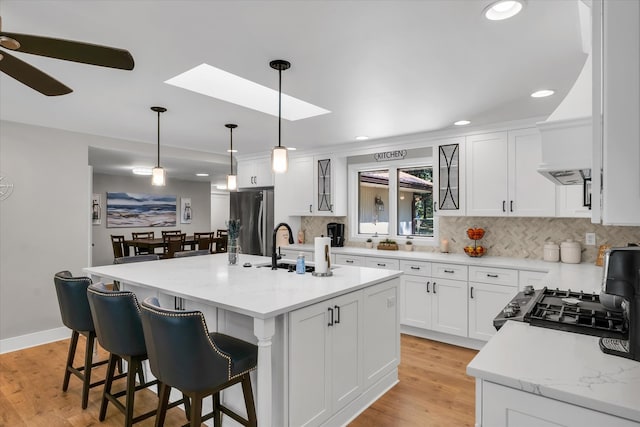 kitchen with a skylight, a kitchen island with sink, stainless steel appliances, and white cabinetry