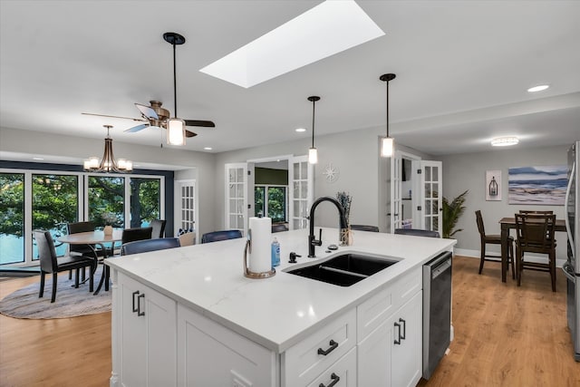 kitchen featuring appliances with stainless steel finishes, white cabinets, a skylight, a kitchen island with sink, and sink