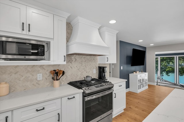 kitchen with custom exhaust hood, backsplash, white cabinetry, appliances with stainless steel finishes, and light hardwood / wood-style floors