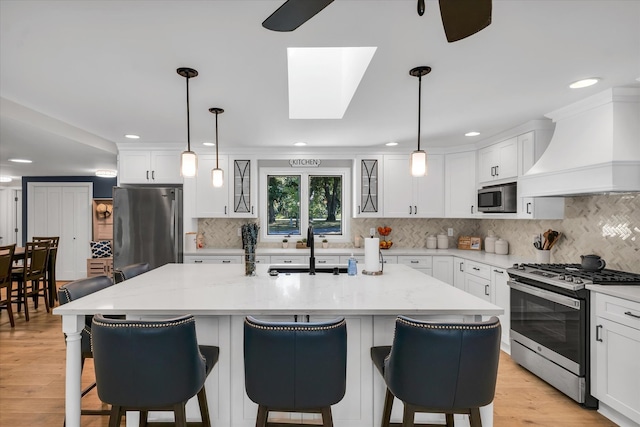 kitchen featuring a center island with sink, a skylight, custom exhaust hood, and stainless steel appliances