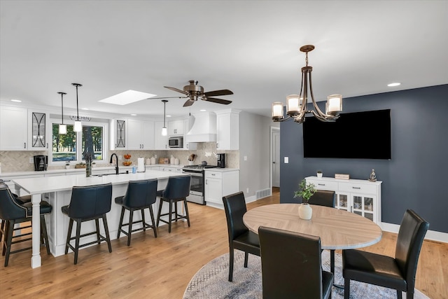 dining area with ceiling fan with notable chandelier, sink, light hardwood / wood-style flooring, and a skylight