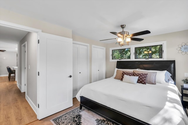 bedroom with ceiling fan, hardwood / wood-style flooring, and two closets