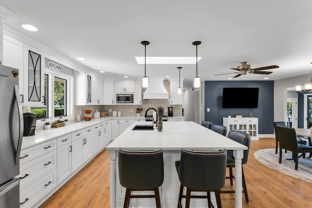 kitchen featuring light wood-type flooring, white cabinetry, a kitchen bar, hanging light fixtures, and stainless steel appliances