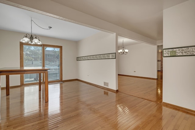 empty room with wood-type flooring and a notable chandelier