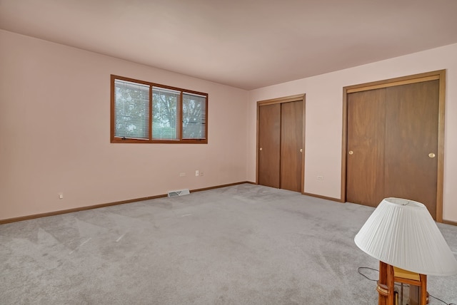 unfurnished bedroom featuring light colored carpet and multiple closets