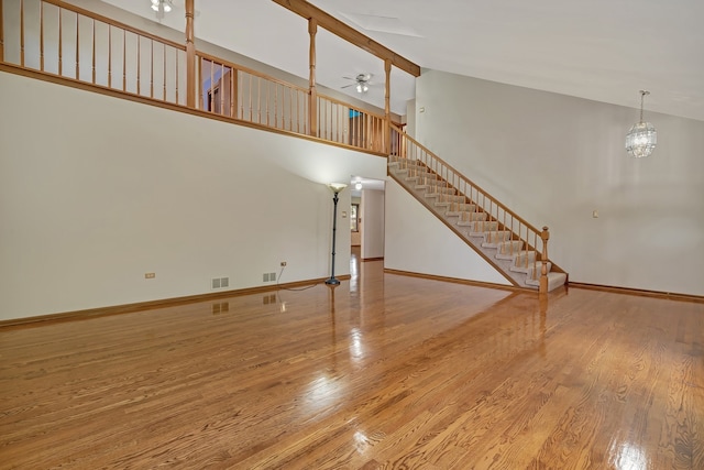 unfurnished living room with high vaulted ceiling, ceiling fan with notable chandelier, and wood-type flooring