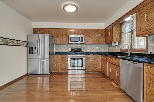 kitchen with appliances with stainless steel finishes, tasteful backsplash, sink, and light hardwood / wood-style floors