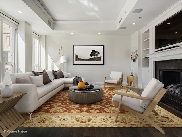 living room featuring a raised ceiling, ornamental molding, built in shelves, and dark hardwood / wood-style flooring