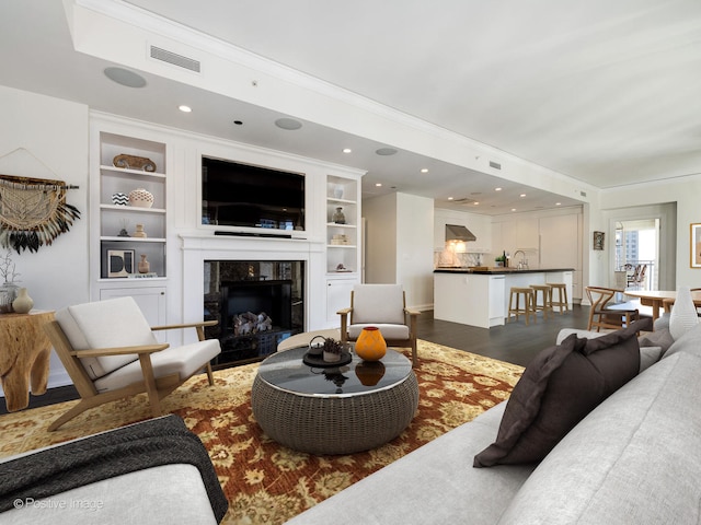 living room featuring ornamental molding, a high end fireplace, built in features, and dark hardwood / wood-style flooring