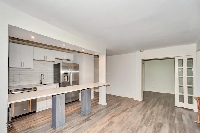 kitchen with sink, tasteful backsplash, light hardwood / wood-style flooring, white cabinetry, and appliances with stainless steel finishes