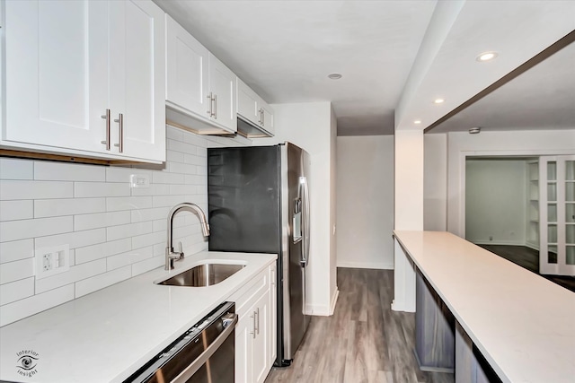 kitchen with appliances with stainless steel finishes, decorative backsplash, white cabinetry, light wood-type flooring, and sink