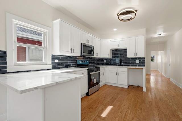 kitchen featuring kitchen peninsula, light stone countertops, stainless steel appliances, light hardwood / wood-style flooring, and white cabinets