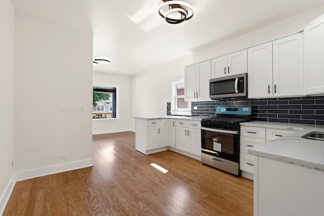 kitchen featuring light stone counters, white cabinets, stainless steel appliances, and light wood-type flooring