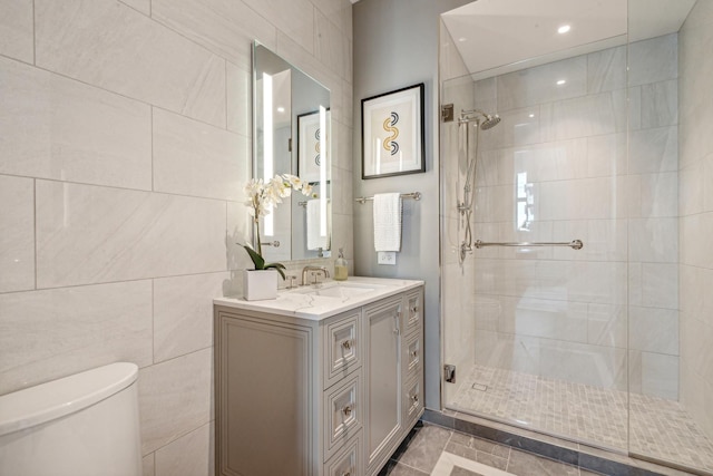 bathroom with toilet, tile patterned floors, vanity, tile walls, and a tile shower