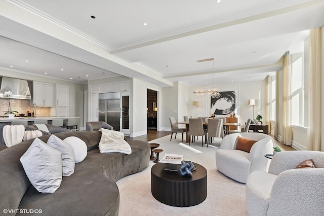 living room featuring sink, light hardwood / wood-style flooring, an inviting chandelier, and crown molding